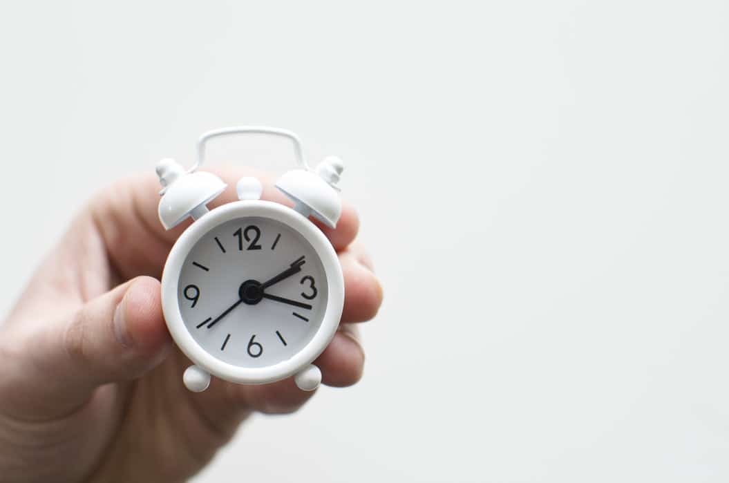Ahorrar tiempo - bob desk software mantenimiento preventivo - pequeño despertador en la mano de un humano, sobre fondo blanco