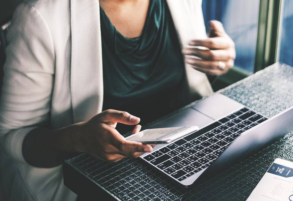 Ahorrar tiempo - bob desk software mantenimiento preventivo - mujer trabajando delante de un macbook y sosteniendo un teléfono móvil